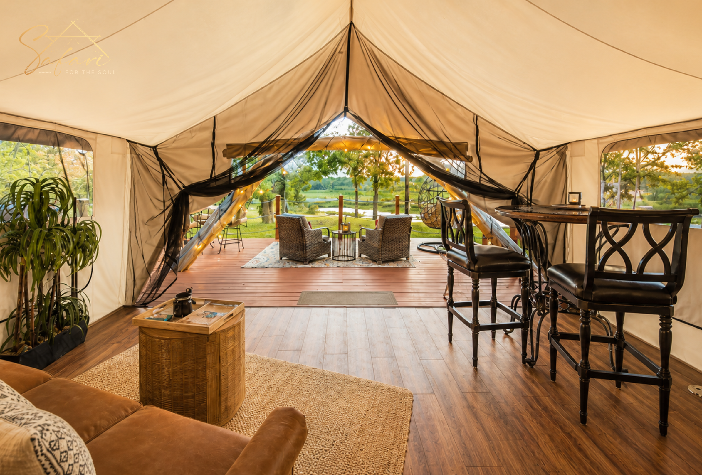 Interior luxury safari tent with open front view, seating area, wooden flooring, and nature backdrop