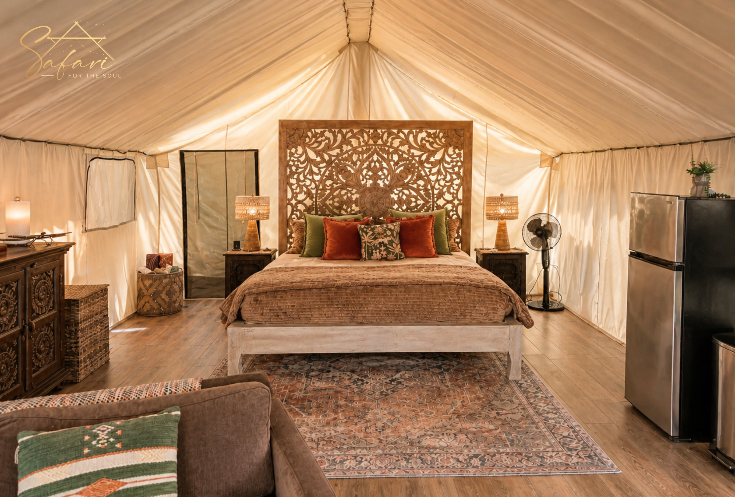 Spacious luxury glamping tent interior with king bed, decorative pillows, mini fridge, fan and rustic furniture in Texas Hill Country