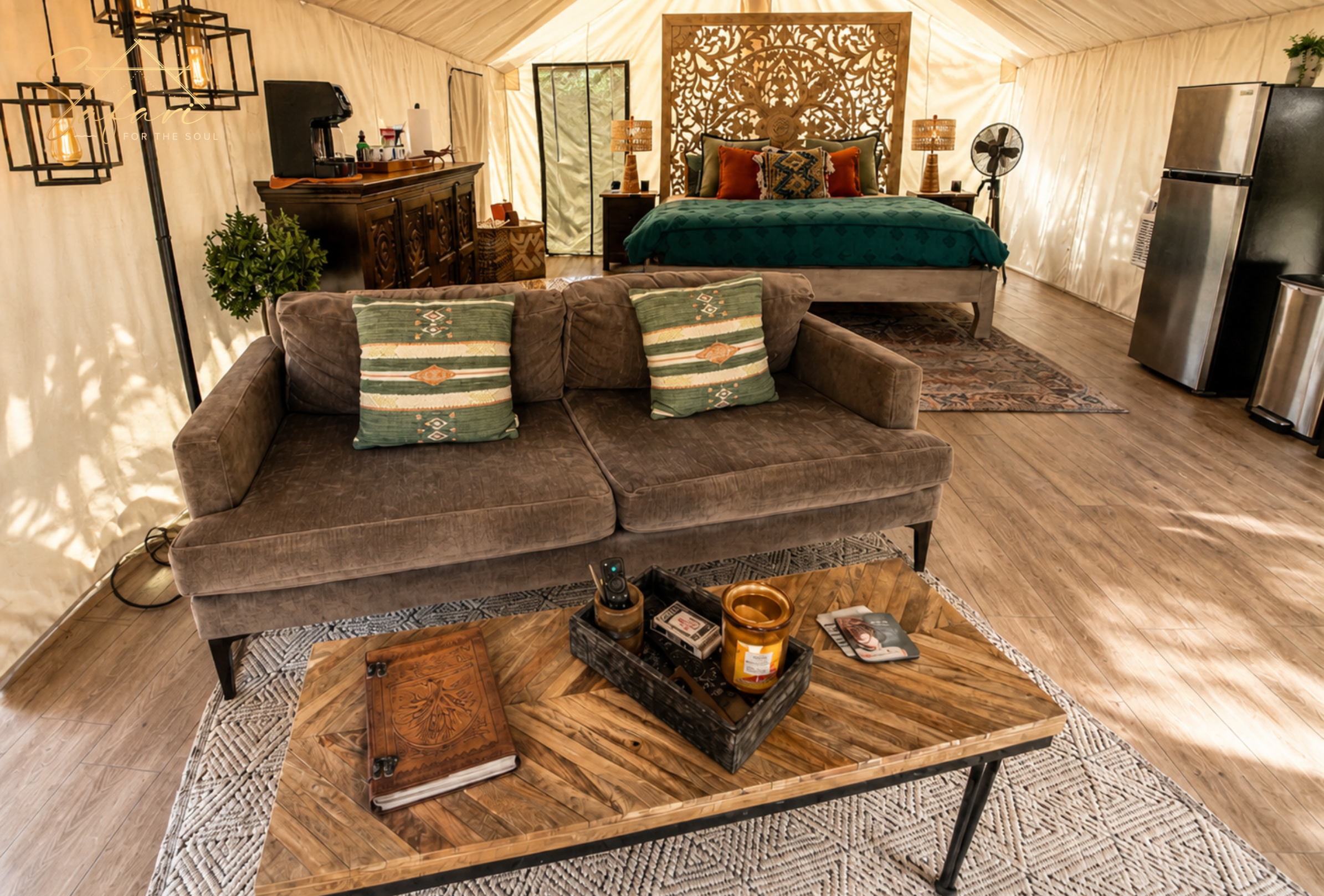 Cozy glamping tent living area with sofa, coffee table, decorative pillows and bedroom setup in background in Marble Falls Texas